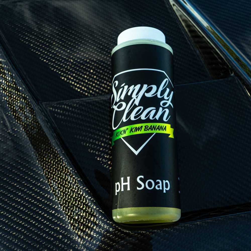Simply Clean Kiwi Banana PH Soap 10 oz Bottle next to a carbon fiber hoodie.